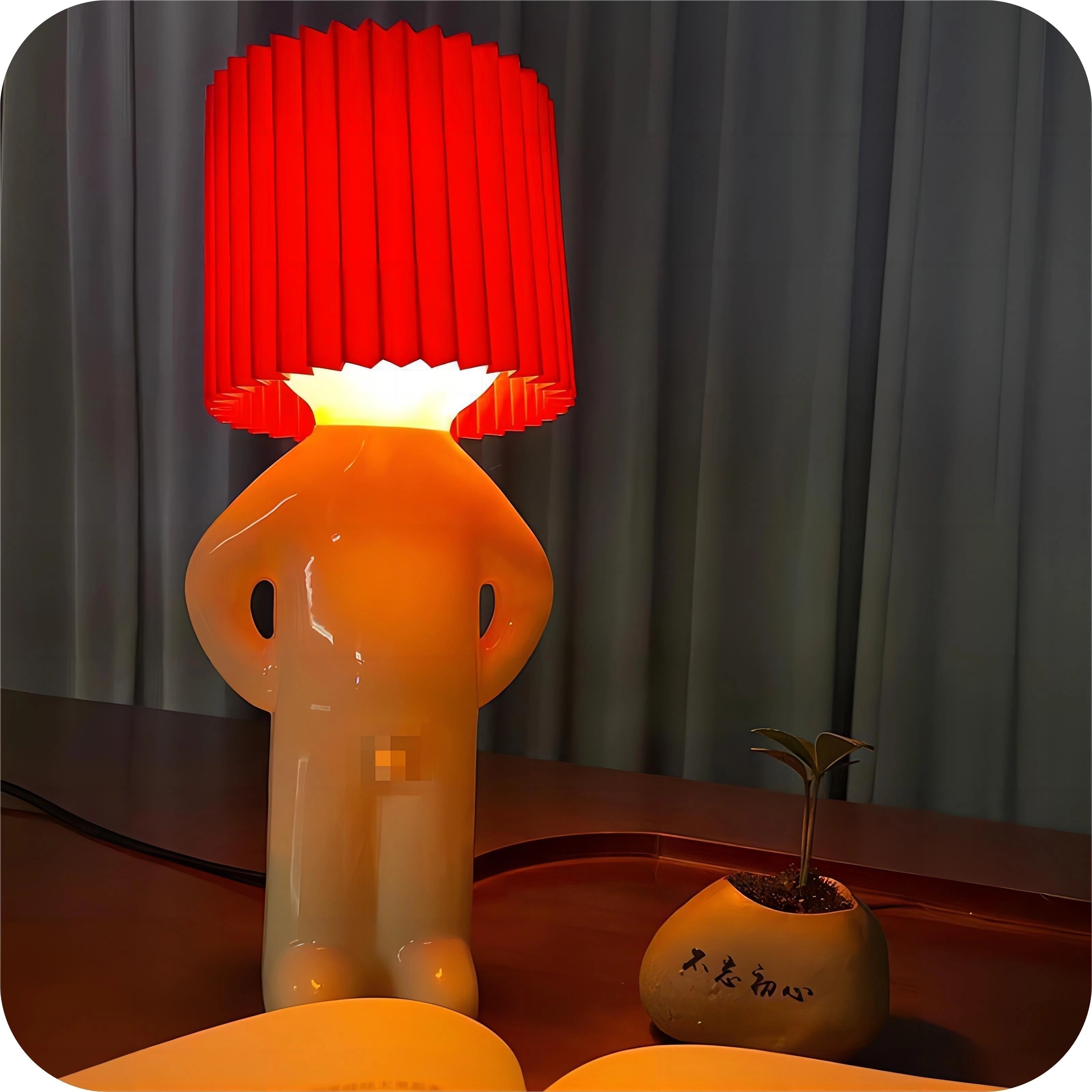 Orange novelty human-shaped table lamp with a quirky design, featuring a rectangular base and cylindrical elements, providing unique accent lighting for home decor.