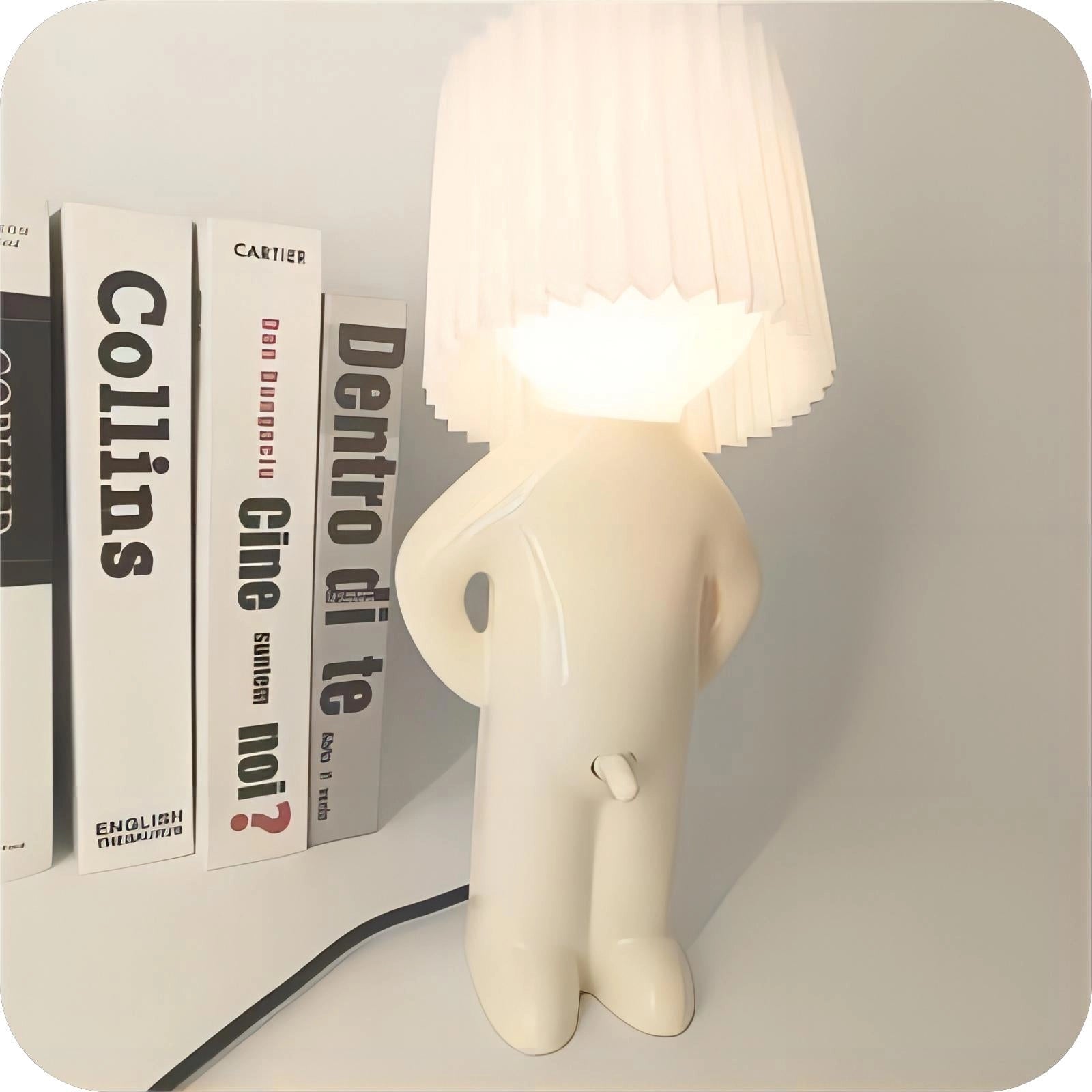 A white novelty human-shaped table lamp with a rectangular base, designed as a quirky accent lighting piece made of plastic material.