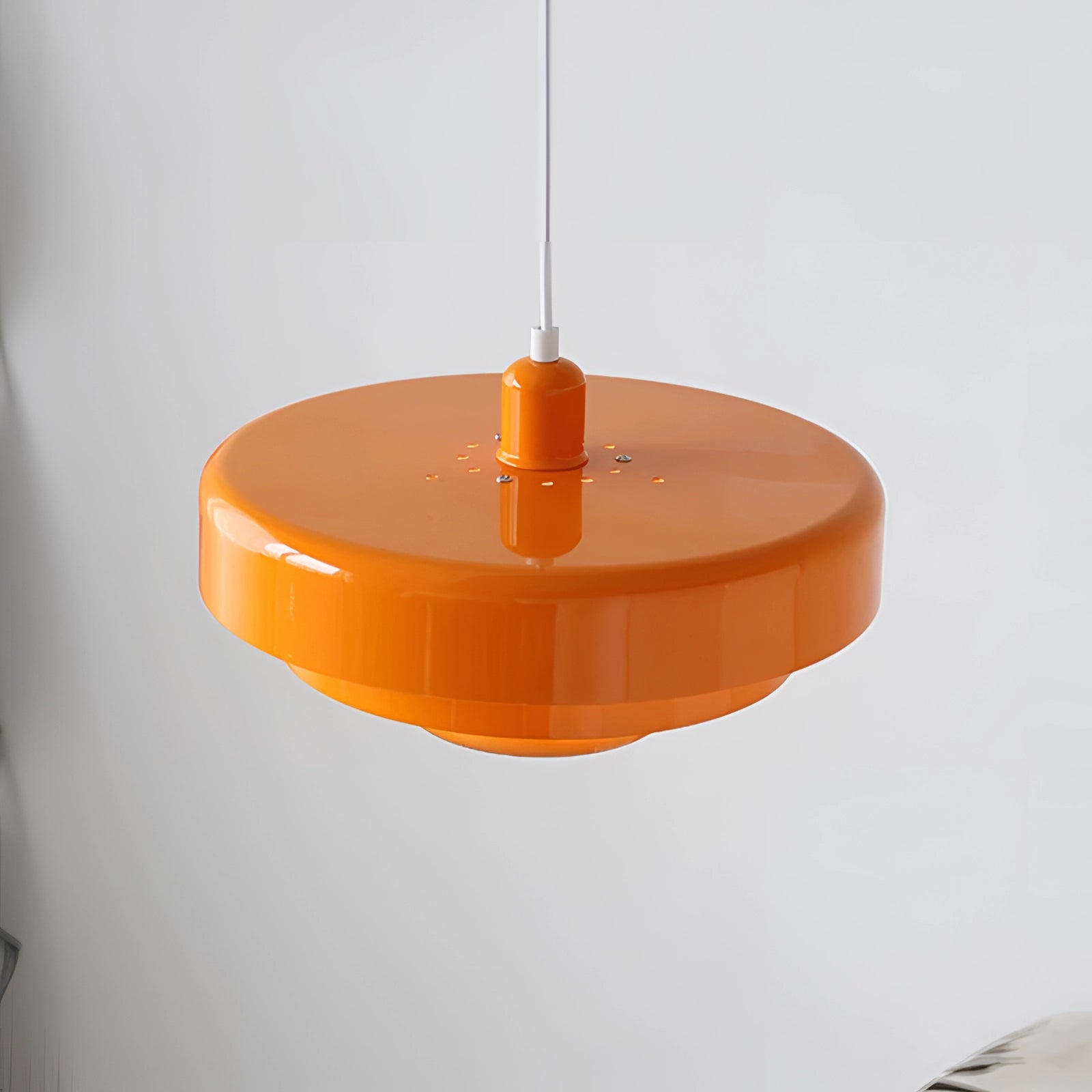 Orange mid-century modern Scandinavian pendant light with a cylindrical shape, featuring a circular ceiling fixture and a transparent design, suitable for interior lighting and decor.
