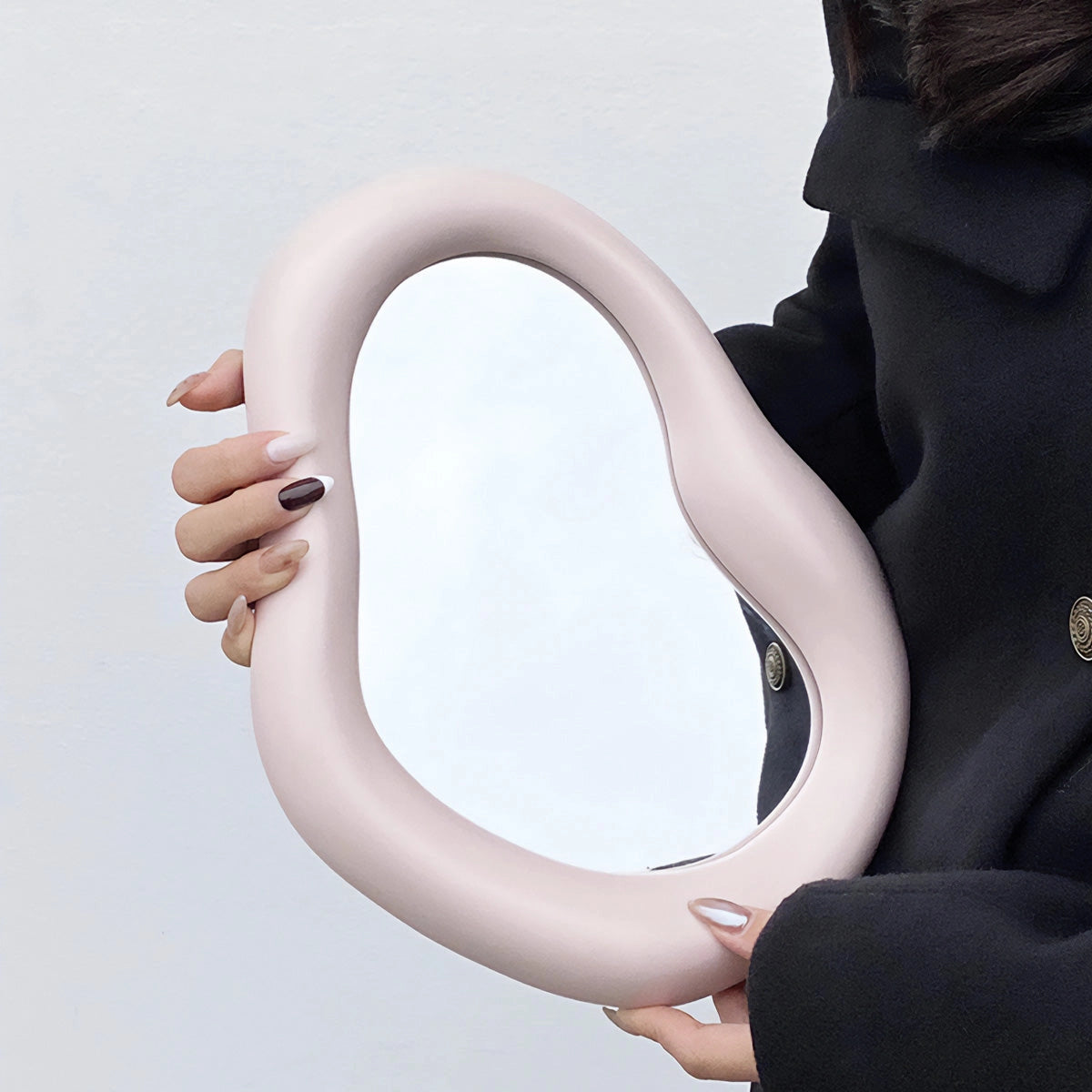 Organic asymmetrical mirror with a modern minimalist design hanging on a wall, reflecting part of a human figure.