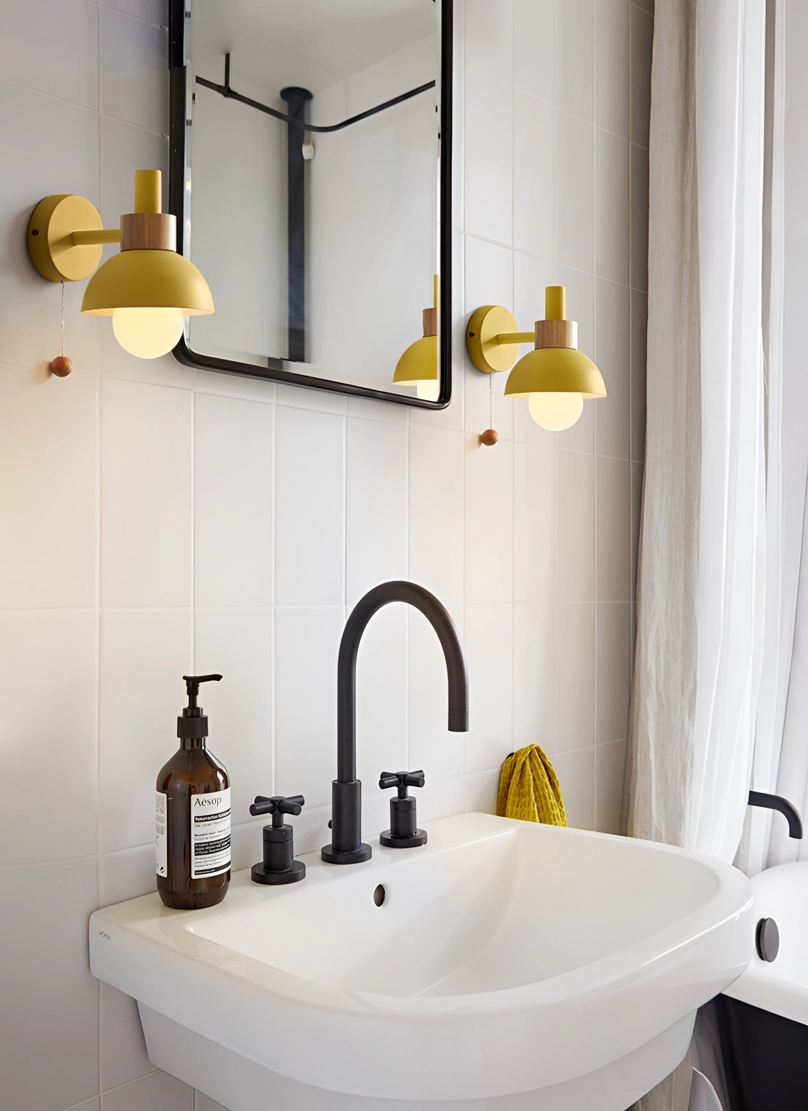 Pastel Scandinavian adjustable wall lamp mounted above a minimalist bathroom sink with a white and wood color scheme, featuring a mirror, tap, and a small potted plant.
