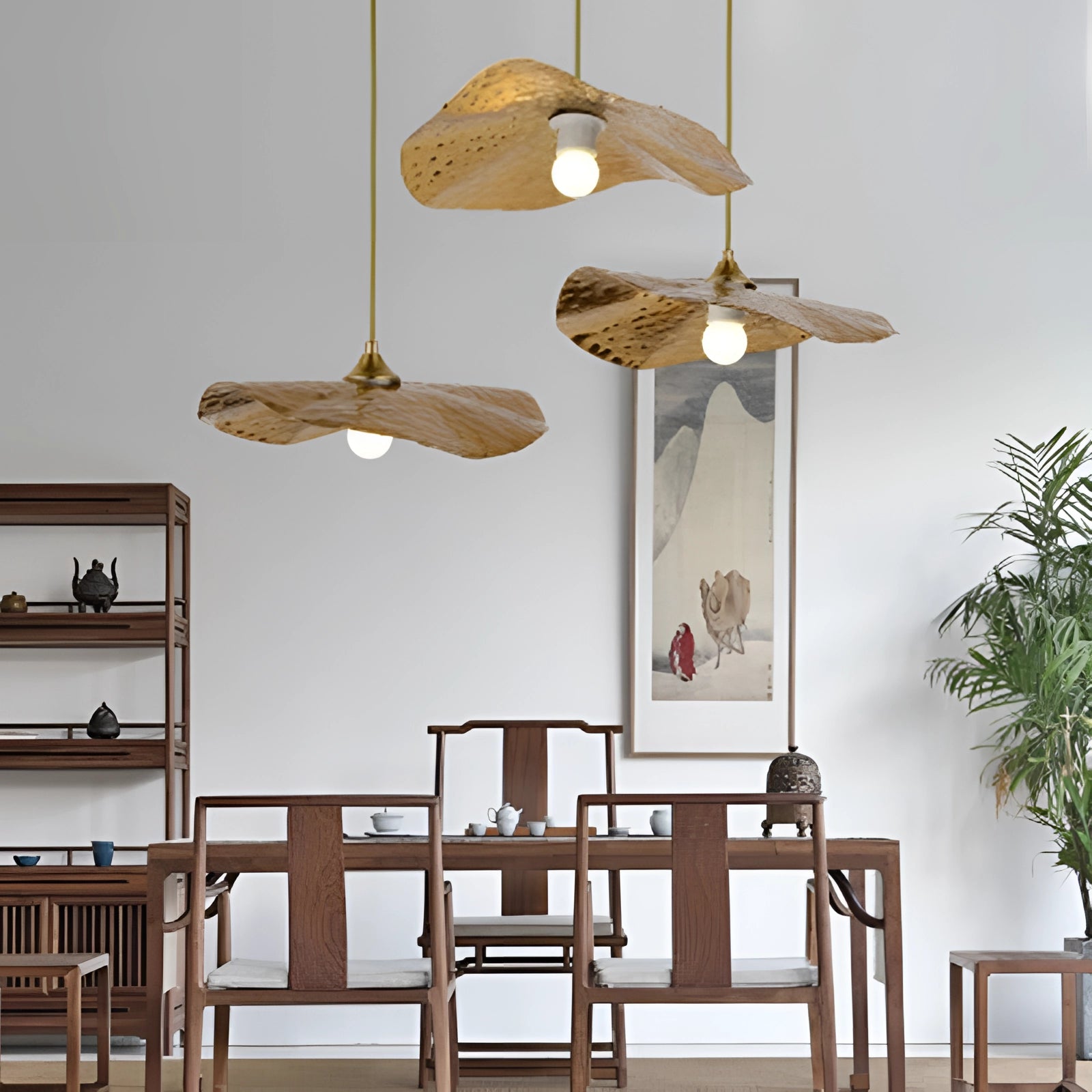 Scandinavian eco-friendly wooden pendant light hanging in a minimalist interior setting with wooden furniture, a small table, houseplants, and a chair against a plain wall.