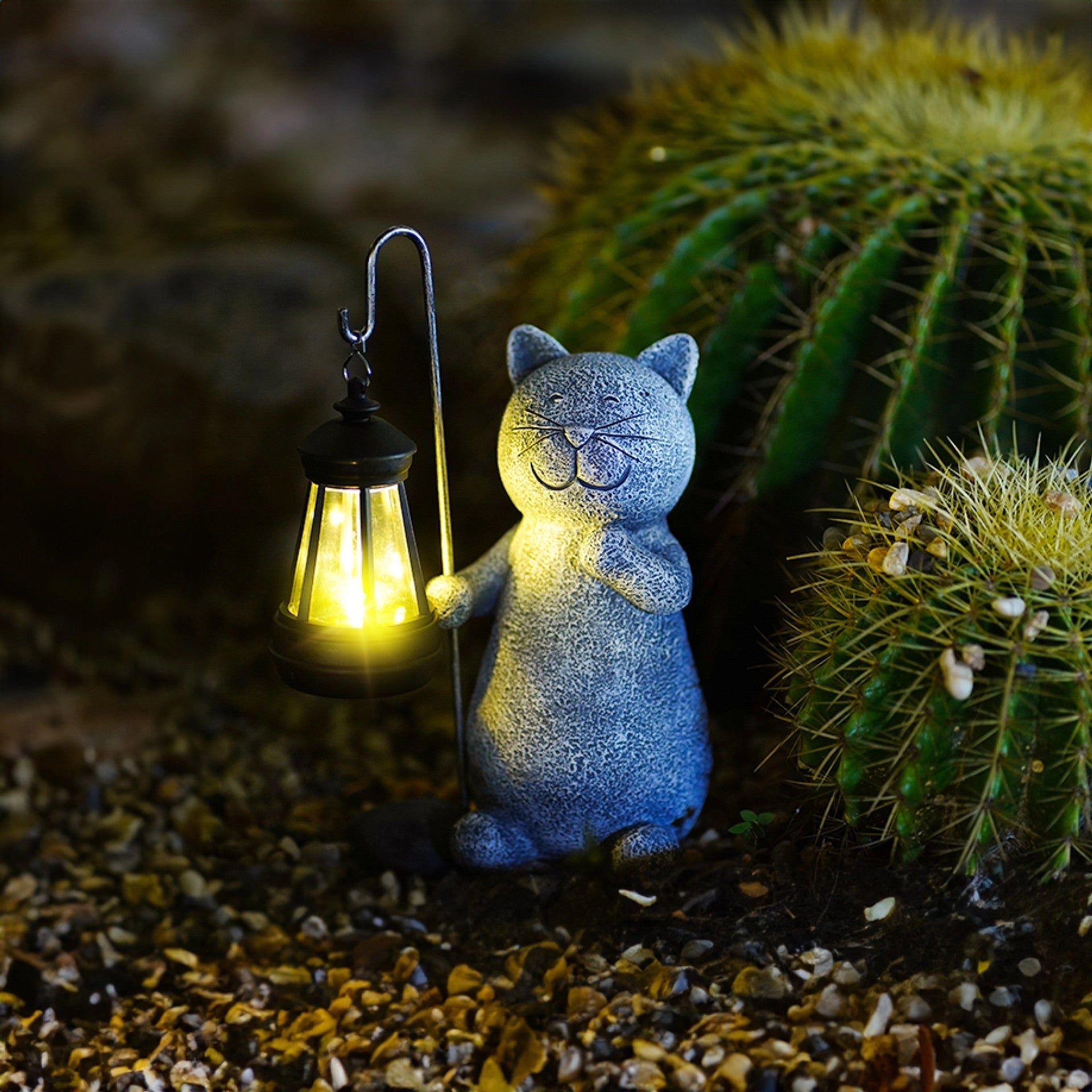 Whimsical eco-friendly solar cat lantern illuminating a garden, surrounded by grass, plants, and trees.