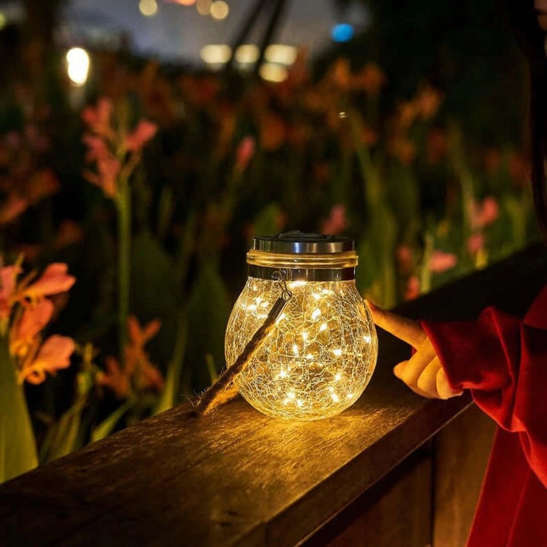 Solar mason jar lights featuring outdoor waterproof LED fairy lanterns, suspended amidst a garden setting with surrounding greenery and wooden elements, casting a soft, warm glow against the backdrop of a clear sky.