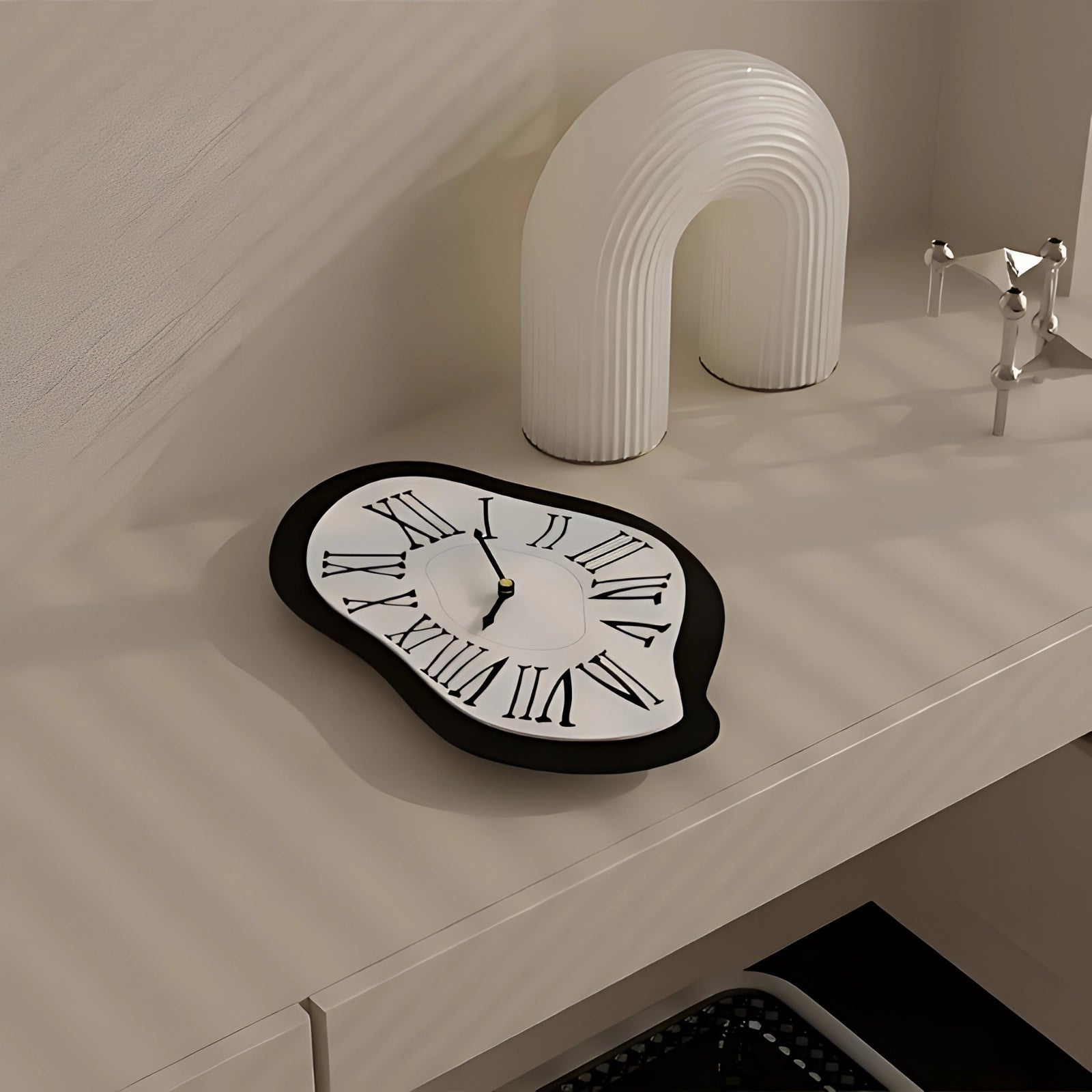 Surreal Salvador Dali melting wall clock with a unique artistic design featuring a distorted, fluid appearance in black and white tones, set against a backdrop suggestive of an interior design setting.