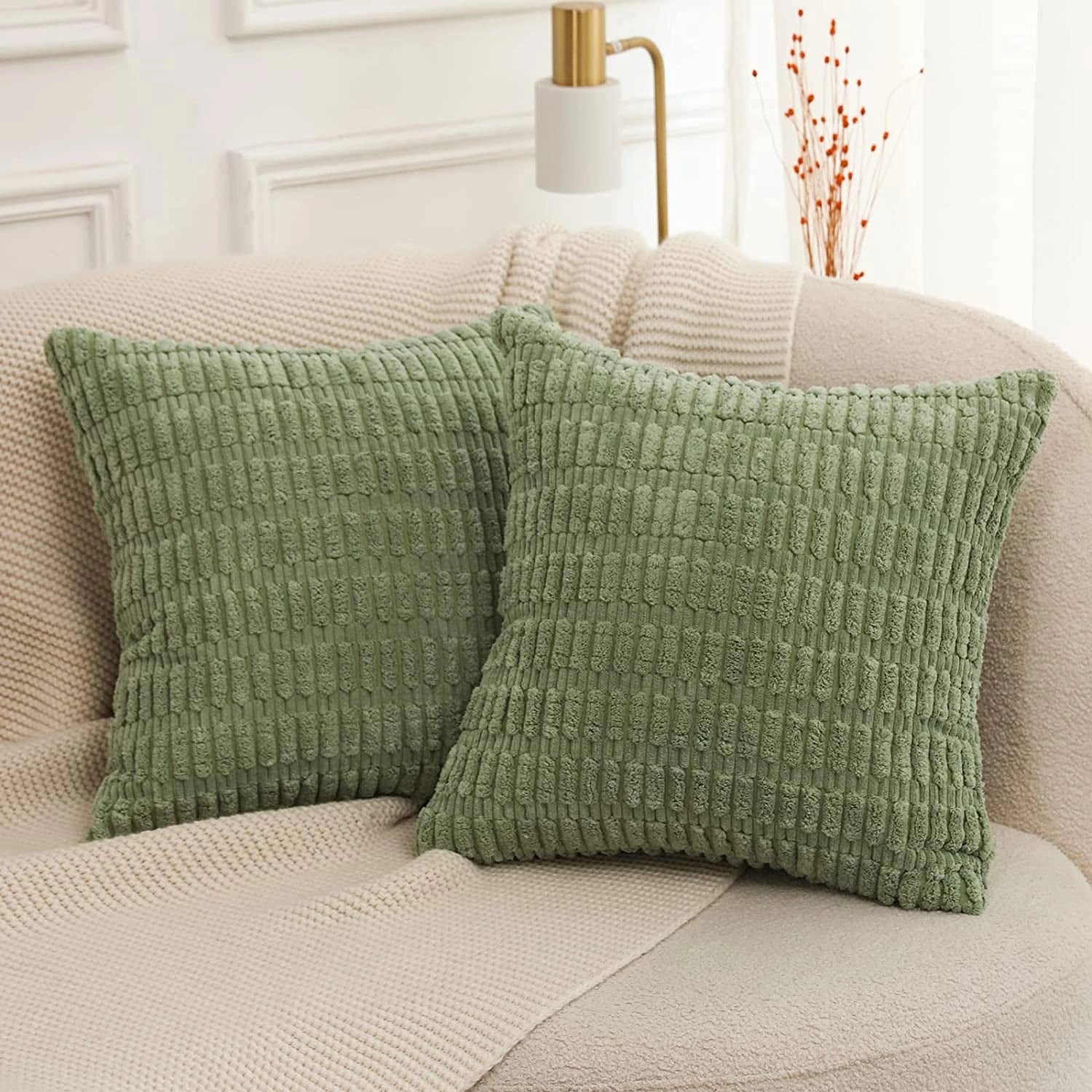 Moss green corduroy cushions in a 45x45cm size, displayed as a 2-pack set on a beige sofa. The cushions add a touch of comfort and style to the interior decor, complemented by wooden flooring.