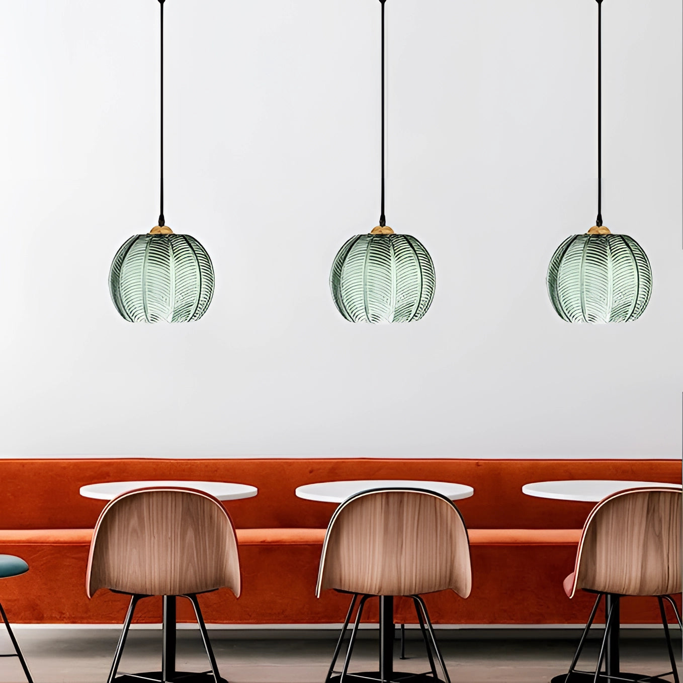 A trio of tropical pendant lights with luxury botanical leaf glass decor, featuring a sleek black and white design, suspended above wooden furniture in a modern interior setting.