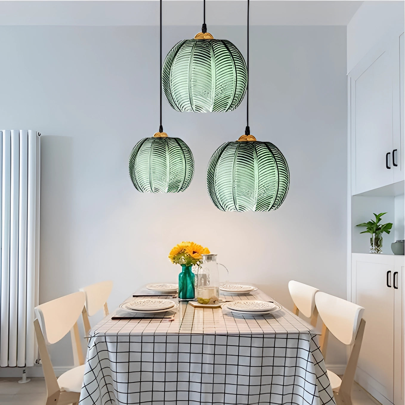 Tropical Pendant Light Trio with luxury botanical leaf glass decor, hanging above a table in a stylish, well-furnished interior setting, showcasing elegant white lighting and lush plant decorations.
