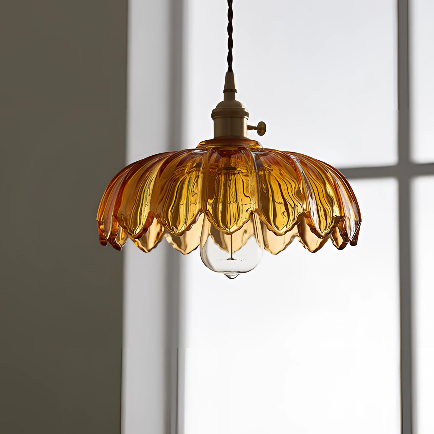 Vintage amber glass pendant light with a brass flower petal design, featuring a warm amber glow and metallic elements, hanging from the ceiling as a chandelier fixture.