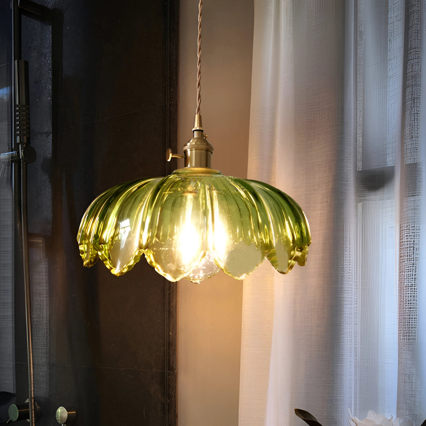 Vintage amber glass pendant light with a brass flower petal design, featuring a green tint, hanging from a ceiling in a stylish interior setting.