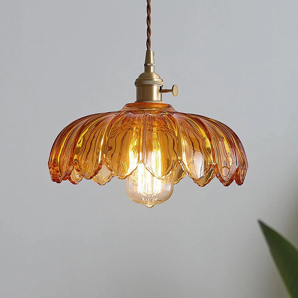 Amber glass pendant light with a brass flower petal design, featuring a spherical chandelier shape and suspended from the ceiling.