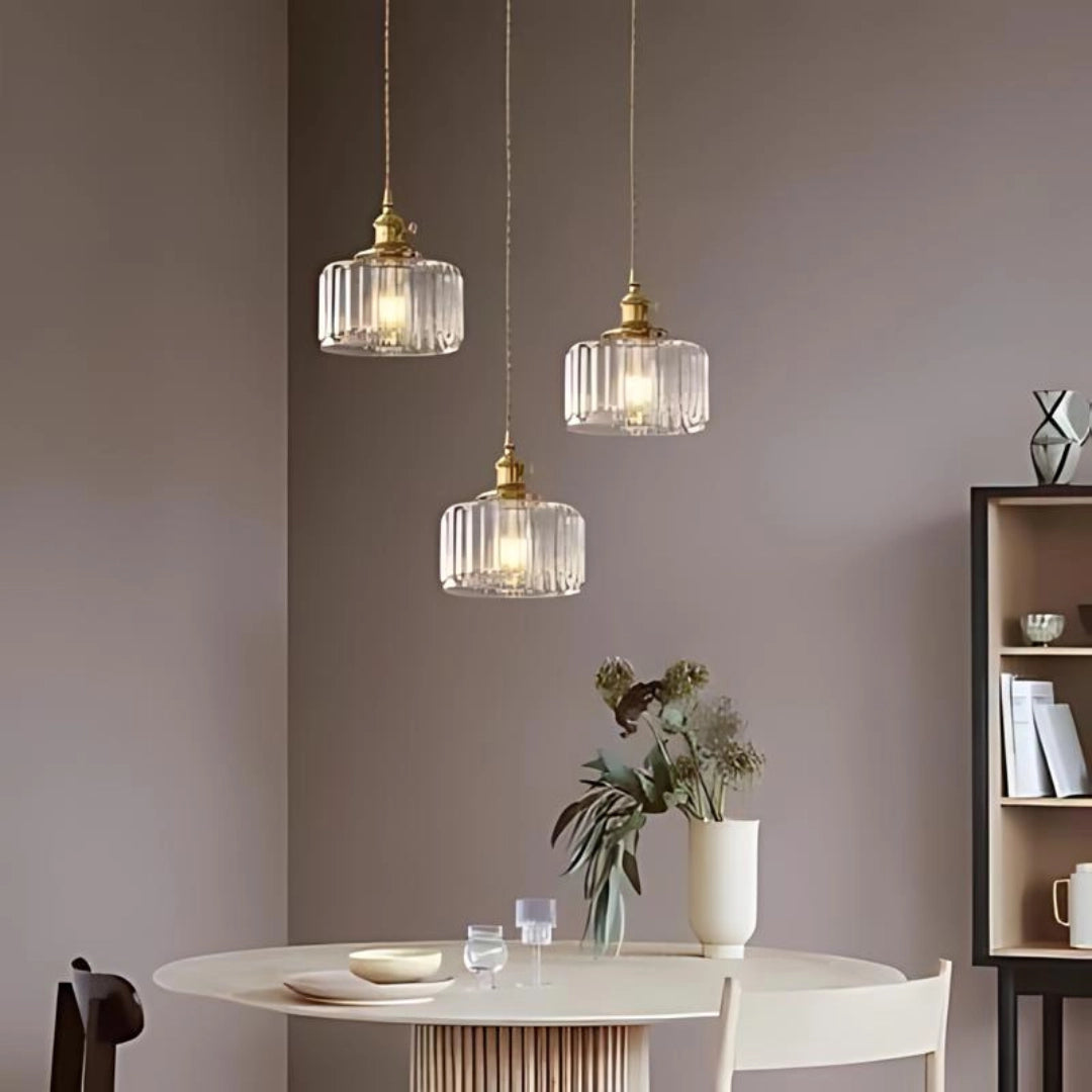 Vintage green glass pendant light with three clear, round ribbed glass heads and antique brass accents, hanging above a wooden table in a stylish interior setting.