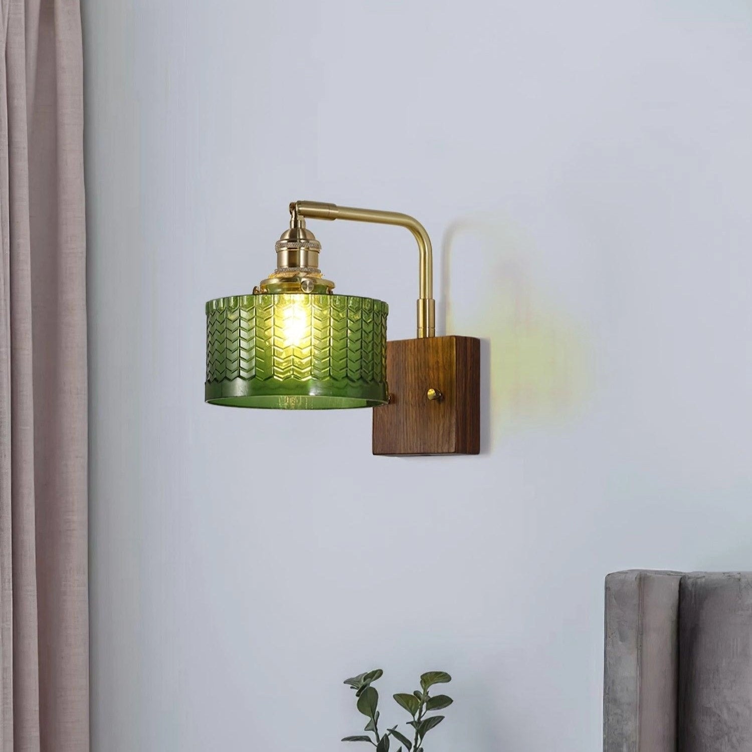 Vintage green glass sconce with a brass arm featuring a fish scale pattern, mounted on a wooden wall.