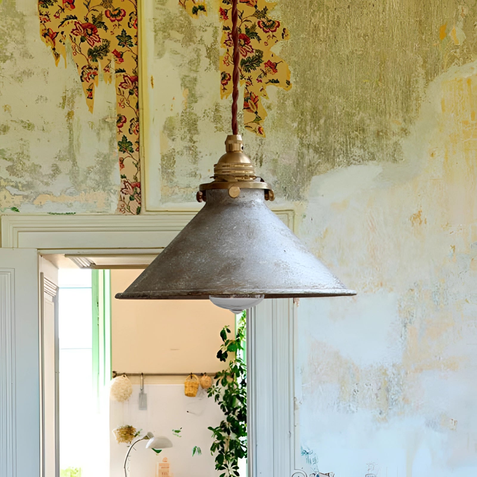 Vintage industrial pendant light fixture with an antique brass and distressed blue finish, featuring a silver shade, suspended in a stylish interior setting with wood accents and greenery.