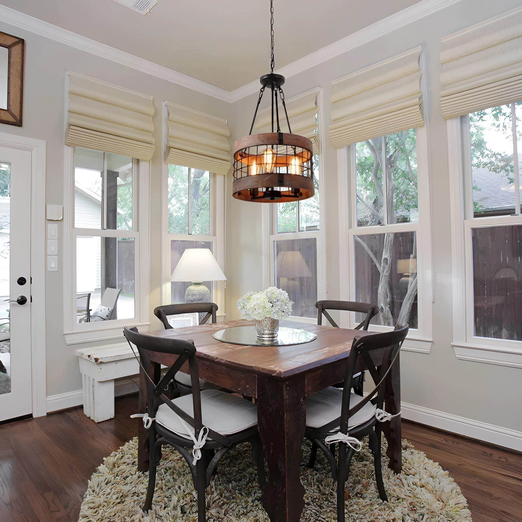 Vintage rustic black wood LED cage chandelier with a 3-light design, hanging in a farmhouse-style interior with visible wooden elements and natural light from a nearby window.