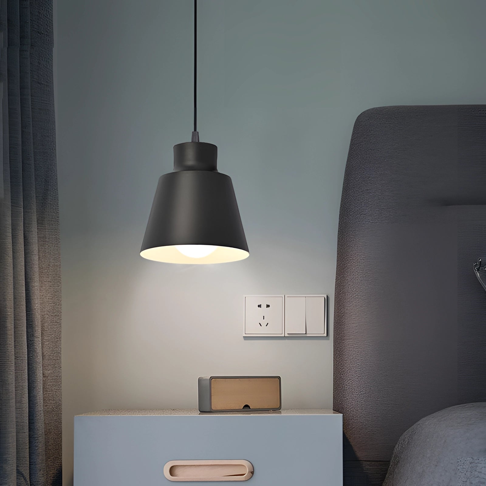 Modern Scandinavian yellow pendant light with a grey shade, illuminating a cozy interior design featuring wood accents and a rectangular wall backdrop.