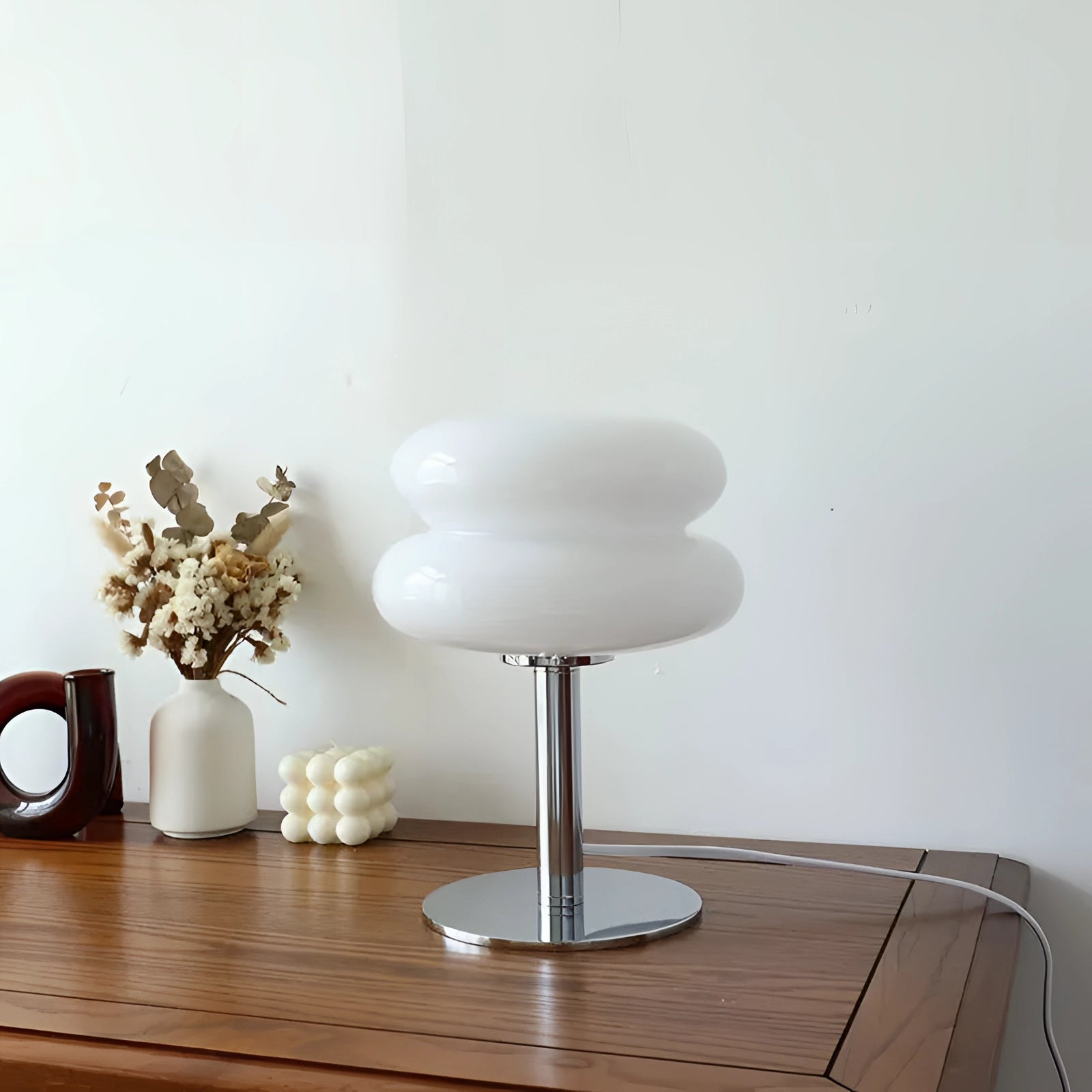 1970s orange mushroom lamp with a chrome base, featuring a modern retro design, placed on a wooden table alongside a white vase and green plant, with a background of shelving.