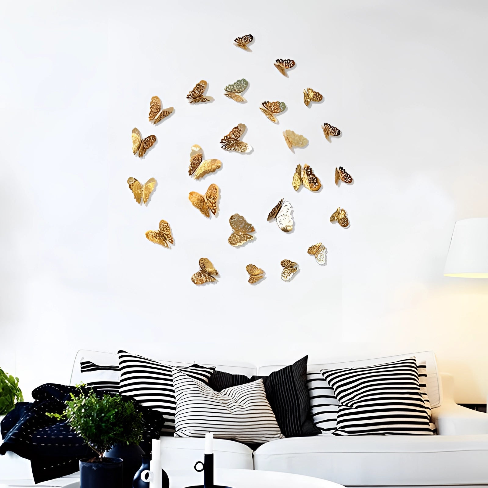 3D gold butterfly wall art displayed in a luxurious living room setting, featuring metallic butterflies creating an elegant sculpture on the wall, with a comfortable studio couch nearby and decorative elements like a flowerpot and lamp.