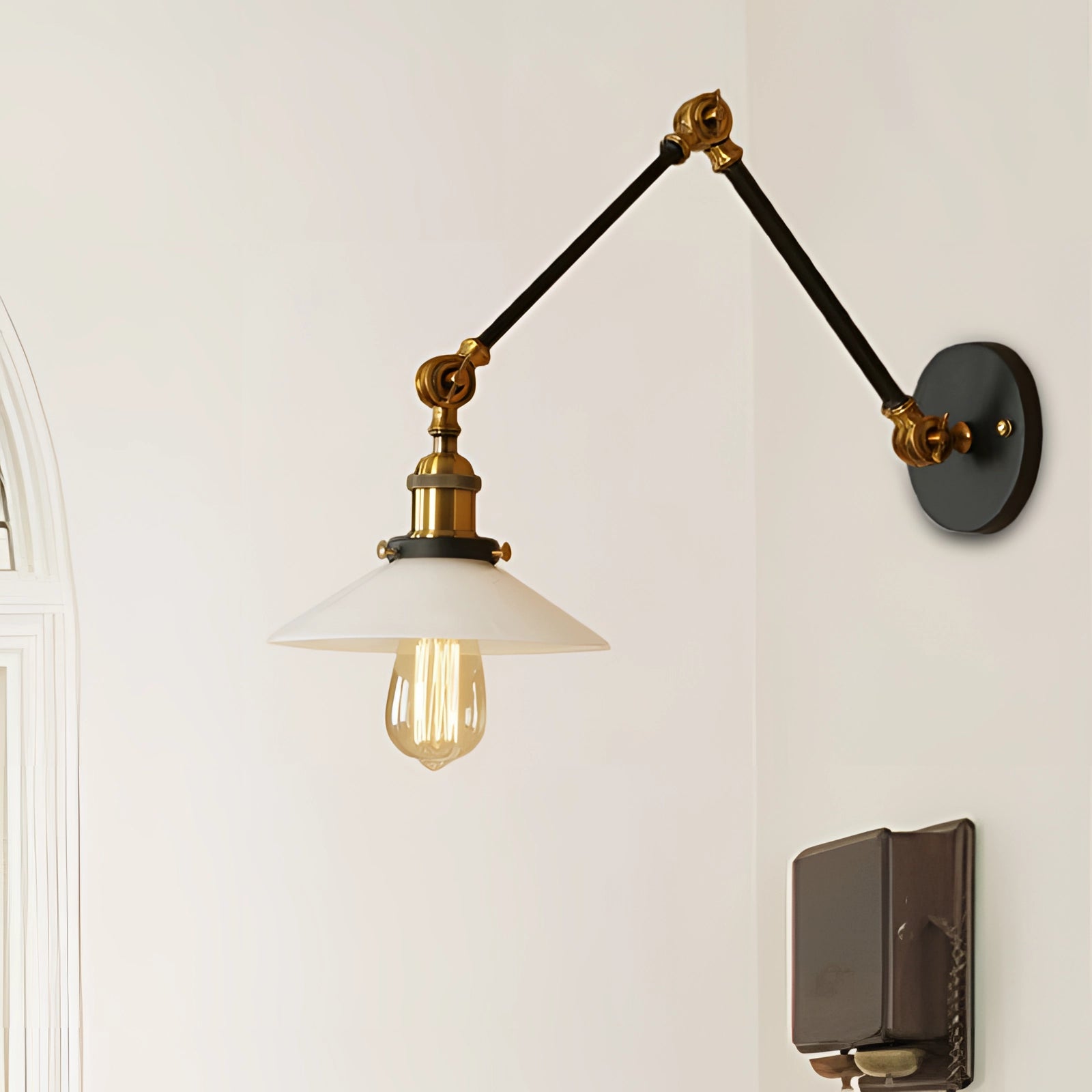 Adjustable vintage brass wall sconce with a frosted glass shade in a bronze finish, featuring a circular design and a visible light bulb, mounted on a wooden wall.