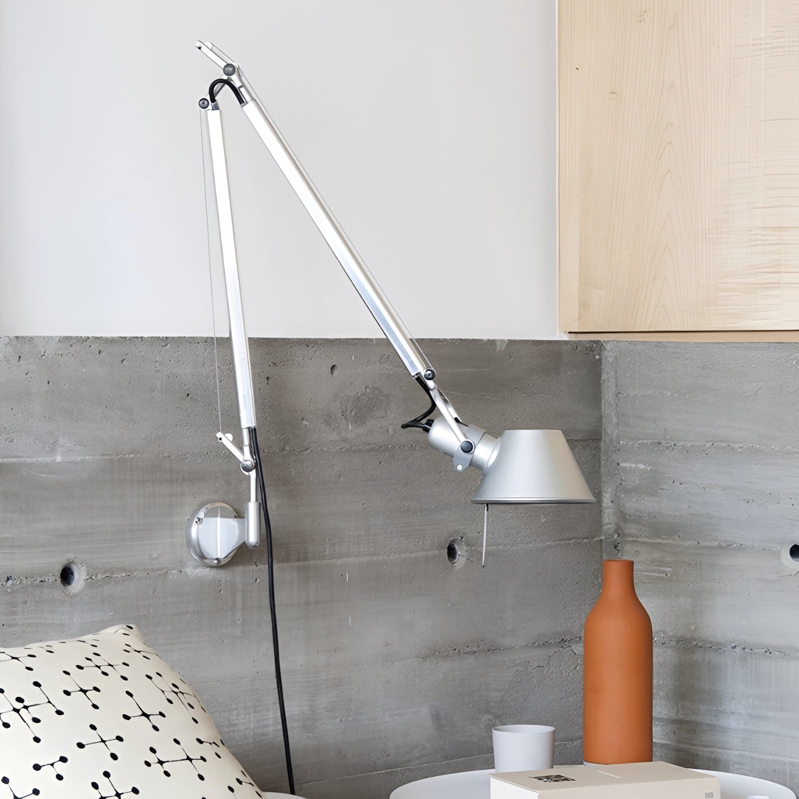 Adjustable wall-mounted metal lamp in an industrial style, featuring a cone-shaped shade, installed on a wooden wall in a room with hardwood flooring.