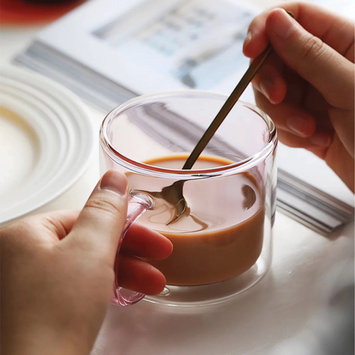 Amber glass mug filled with coffee, held by a hand, showcasing its durable and heat-resistant design, placed on a table.