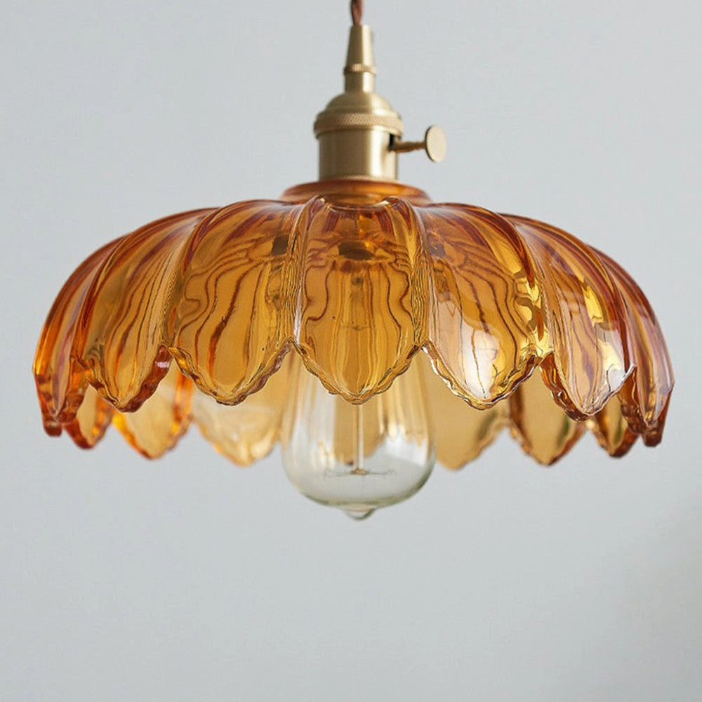 Amber glass pendant light with vintage flower design and antique brass finish hanging from ceiling.