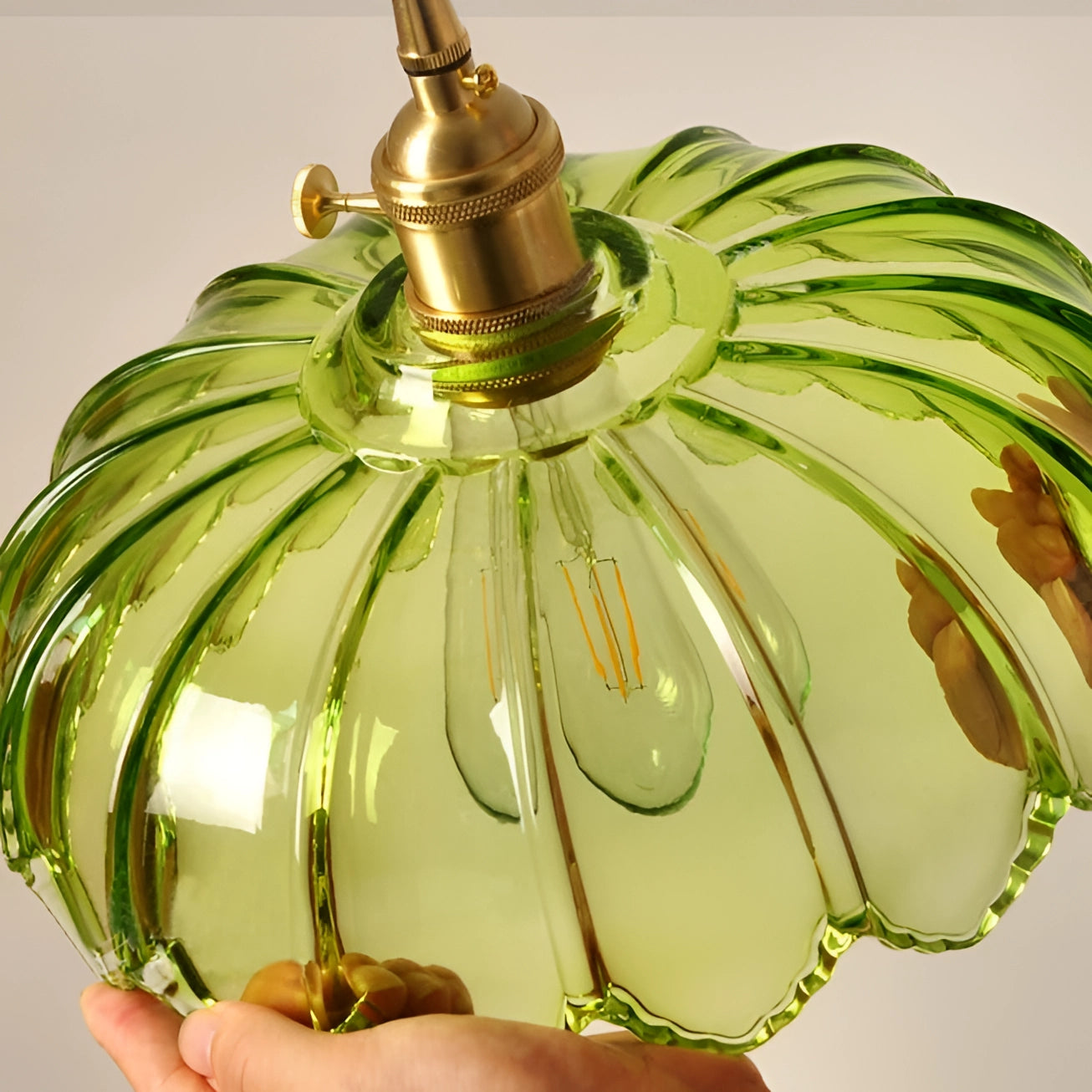 Amber glass pendant light with vintage flower design and antique brass finish, hanging amidst green plants and decorative ornaments.