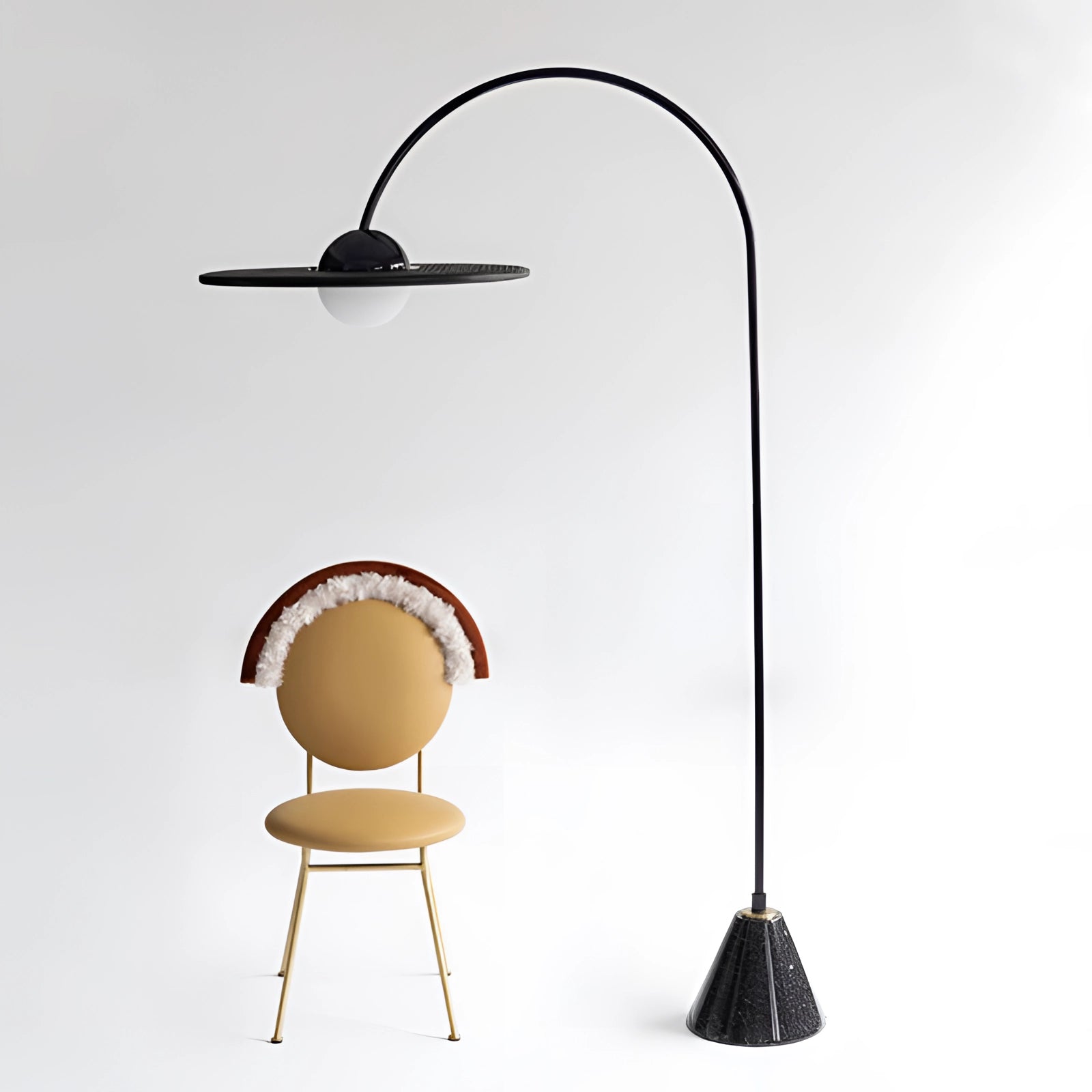 Arched Minimalist Floor Lamp in modern black with a sculptural design, positioned in a contemporary interior setting featuring a wooden floor, chair, and table.