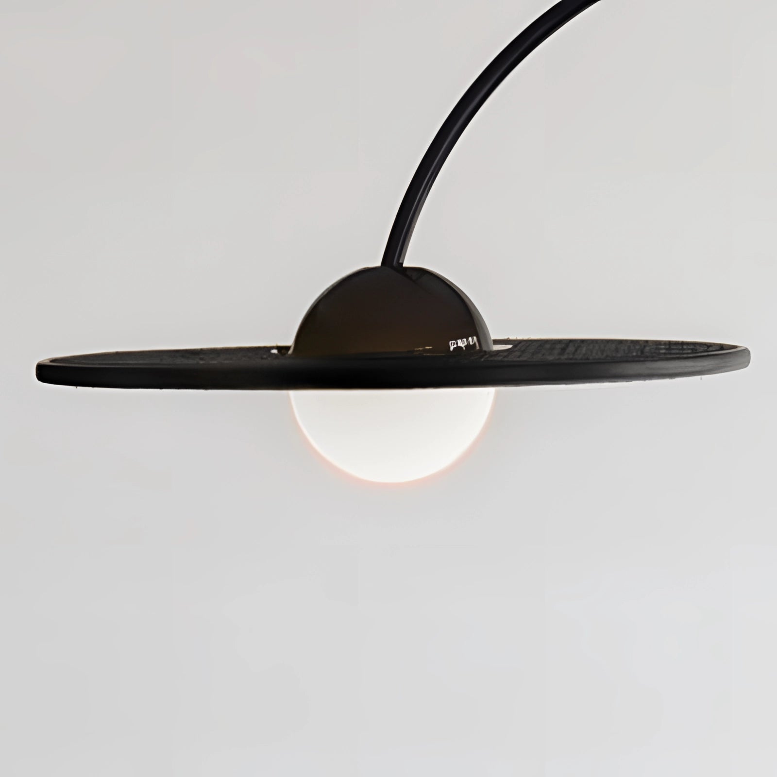 A modern black arched minimalist floor lamp with a sculptural design, featuring a sleek metal finish, standing on a wooden base. The lamp is placed in a contemporary setting, casting light over a table.