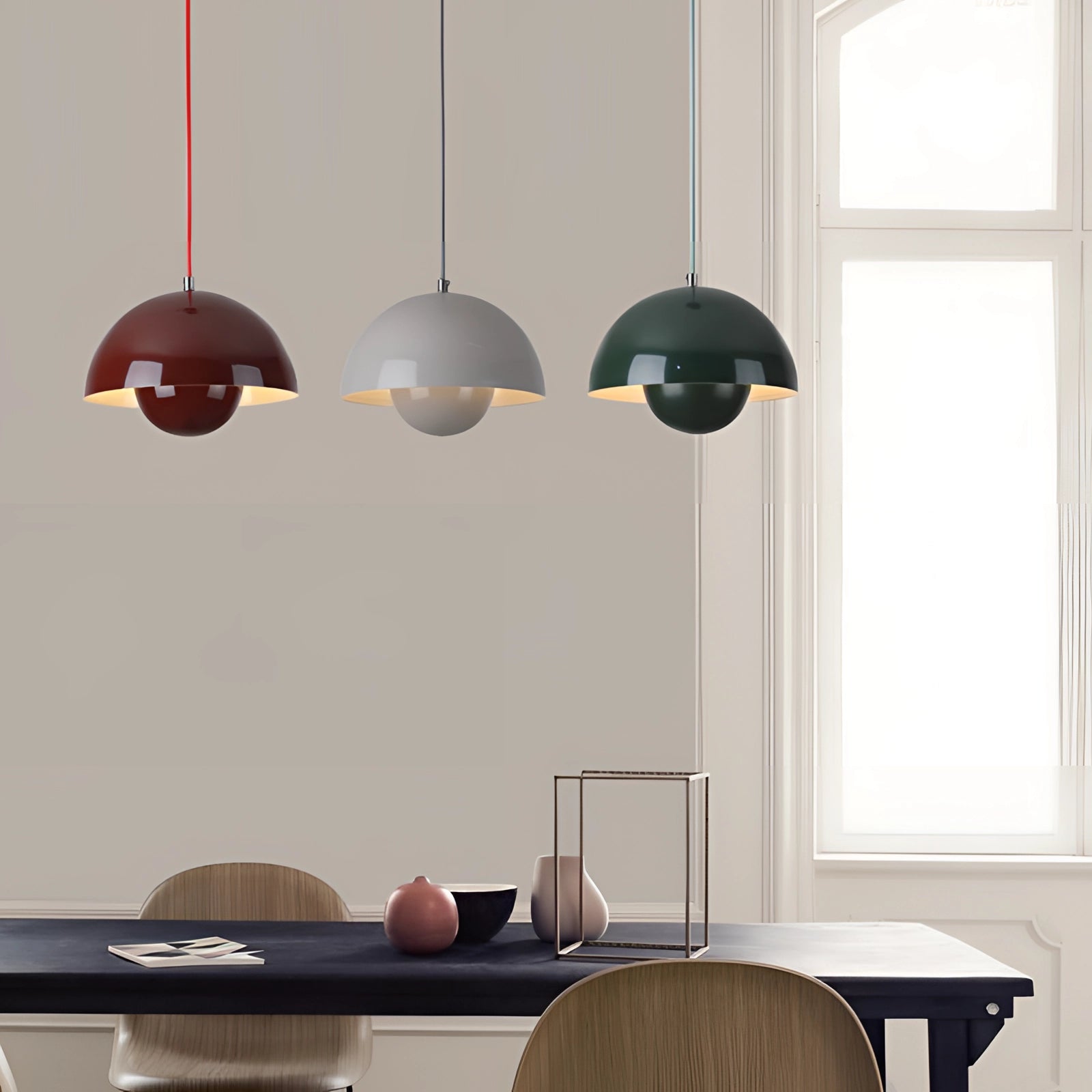 Modern retro pendant lights in yellow, white, and orange colors hanging above a wooden table near a window, showcasing interior design elements.