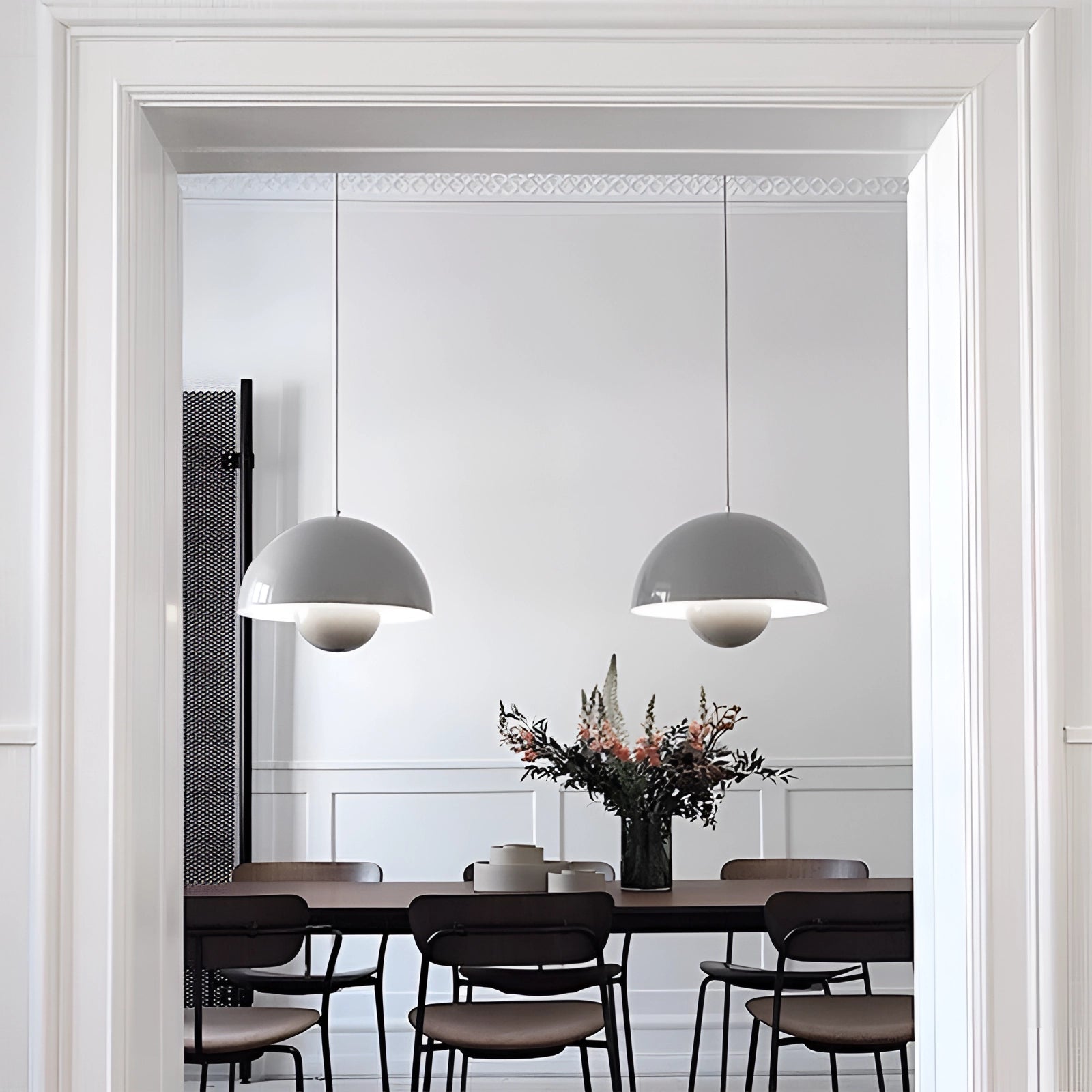 Modern retro pendant lights in yellow, white, and orange hanging above a wooden table with chairs, plants, and stylish interior decor in the background.