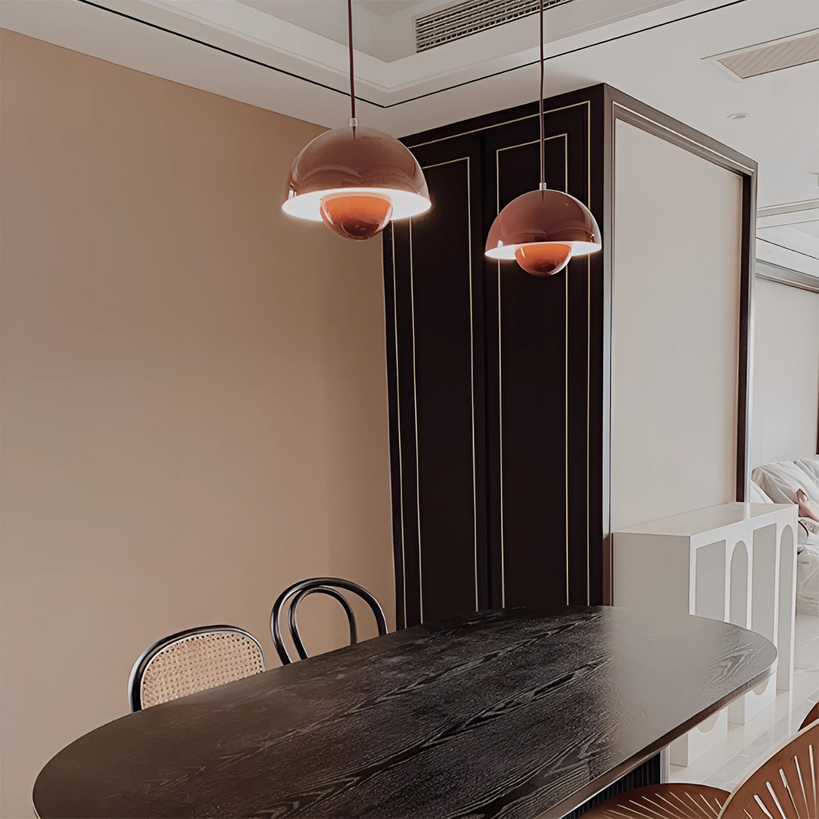 Modern retro pendant lights in yellow, white, and orange hanging from the ceiling above a wooden table and chairs in a stylishly designed interior space.