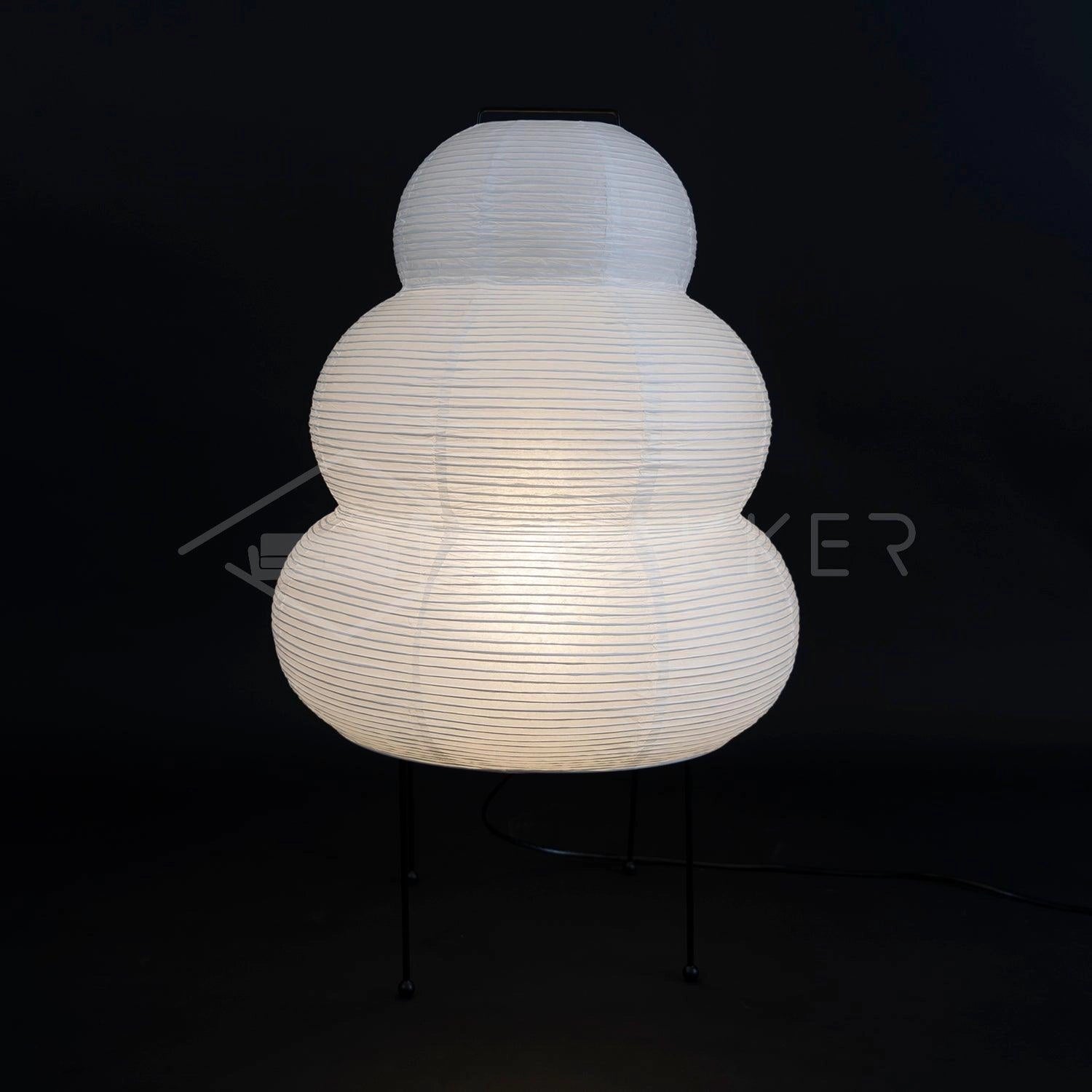 A unique Beehive sculptural tripod floor lamp with a circular lampshade, designed to be a statement lighting piece, casting shadows in the darkness.