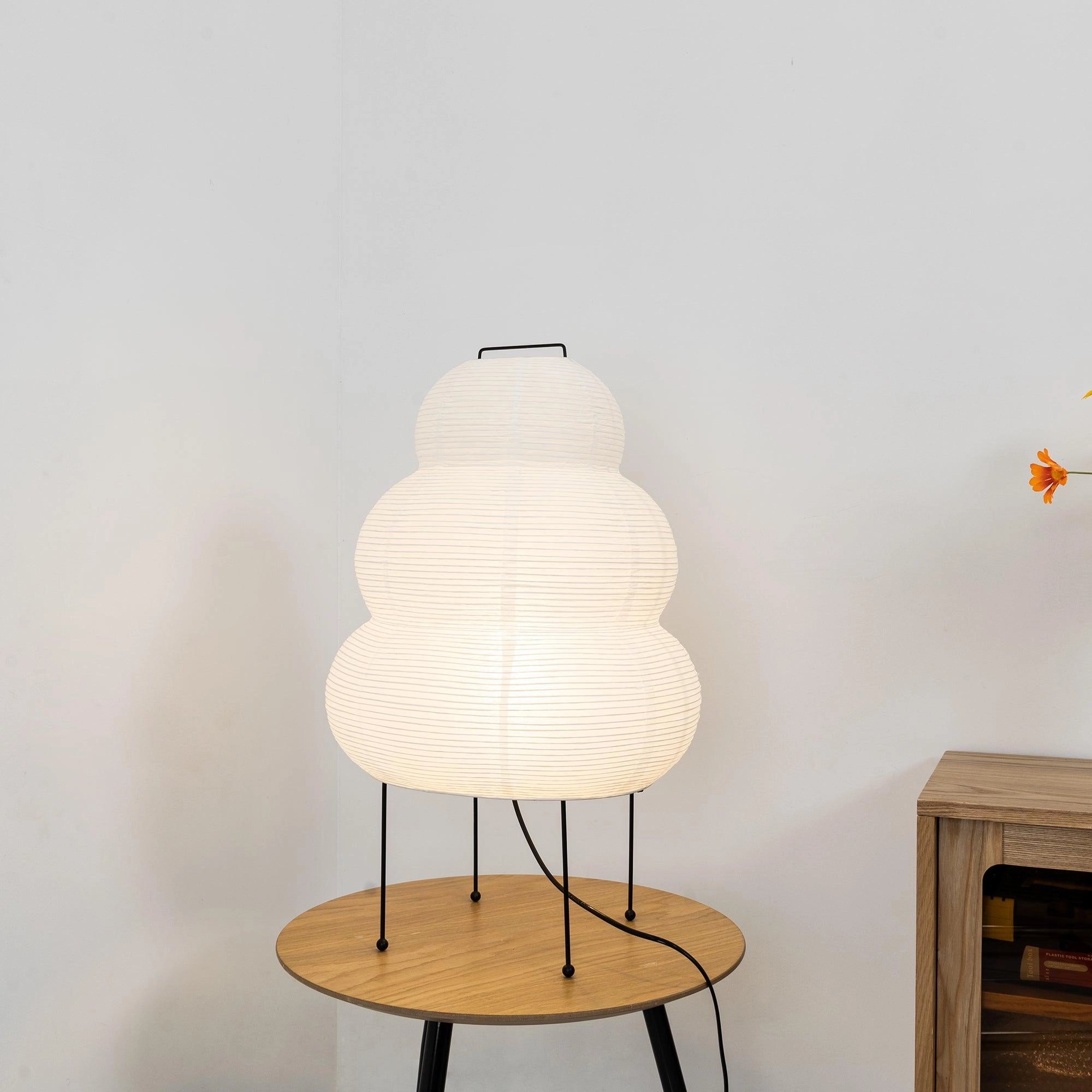 Unique Beehive Sculptural Tripod Floor Lamp in a living room setting with wooden furniture, including a table and shelving, providing ambient lighting.