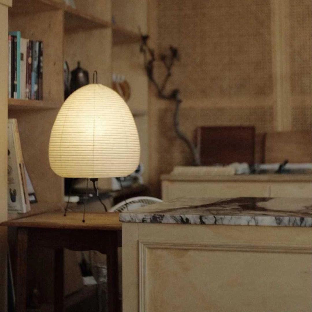 Unique beehive sculptural tripod floor lamp in a living room setting with wooden flooring, cabinetry, and shelving in the background.