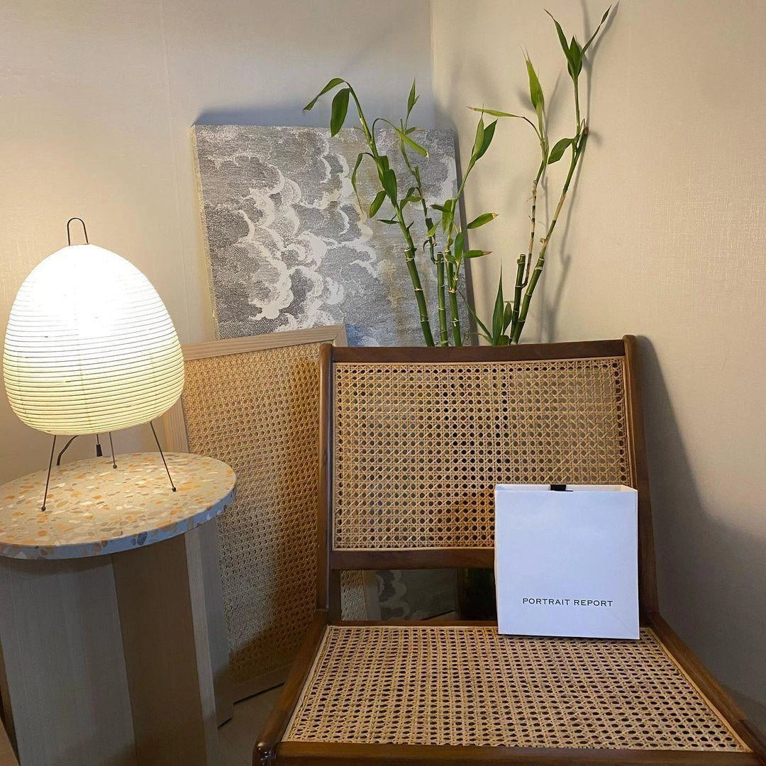 A unique sculptural tripod floor lamp designed like a beehive, placed in a stylish interior setting with wooden furniture, plants, and a rectangular table.