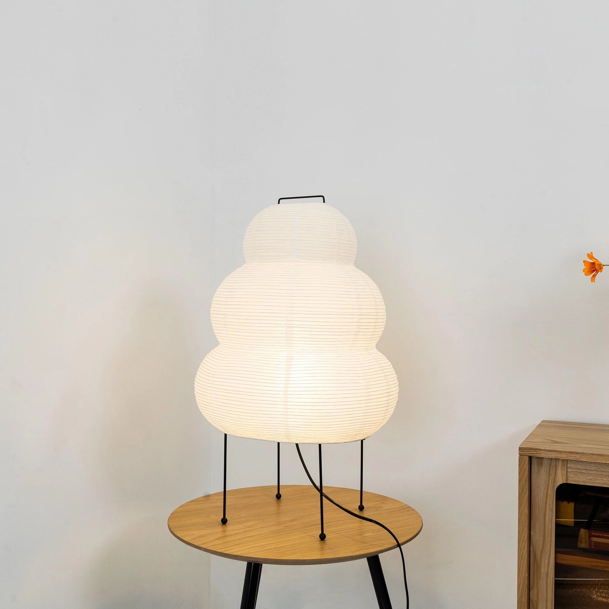 Unique Beehive Sculptural Tripod Floor Lamp with wooden legs, artistic design, and circular shade, placed near a table with shelving in the background and a ceiling fixture above.