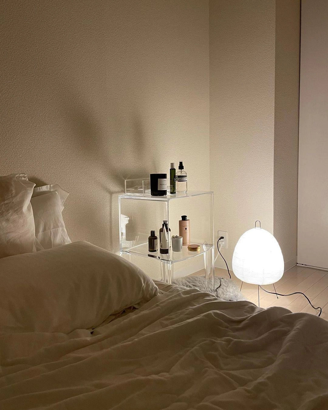 Unique sculptural tripod floor lamp with beehive design, featuring wooden legs and a grey shade, placed in a contemporary interior setting with beige flooring and neutral wall.