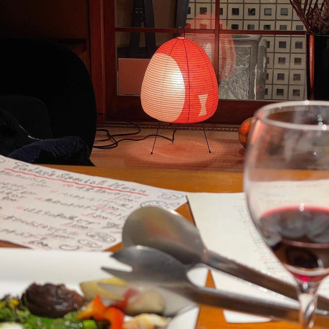 A unique sculptural tripod floor lamp designed to resemble a beehive, positioned in a modern living space with a table set for drinks, including wine glasses and barware.