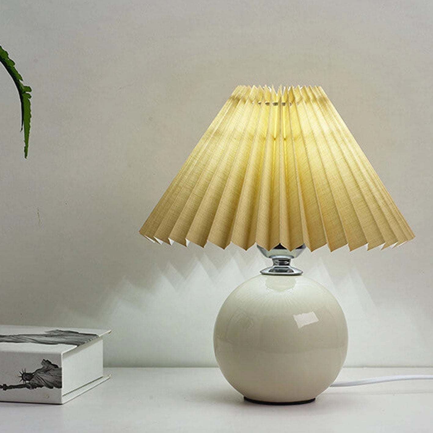 Beige ceramic table lamp with an accordion pleated shade, featuring a sleek design suitable for interior decoration.