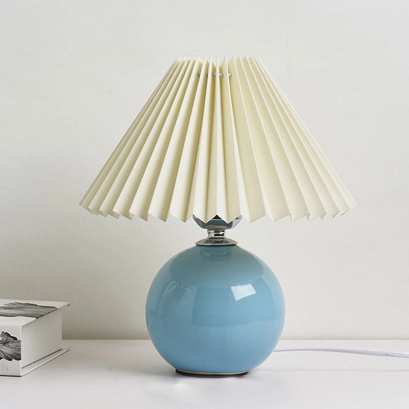 Beige ceramic table lamp with accordion pleated light blue shade and pushbutton switch on a wooden base.