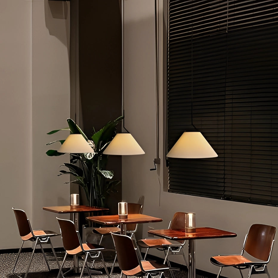 A beige Scandinavian cone pendant light hanging above a minimalist dining table with wooden chairs and a potted plant, featuring modern interior design elements including floor-to-ceiling window blinds.