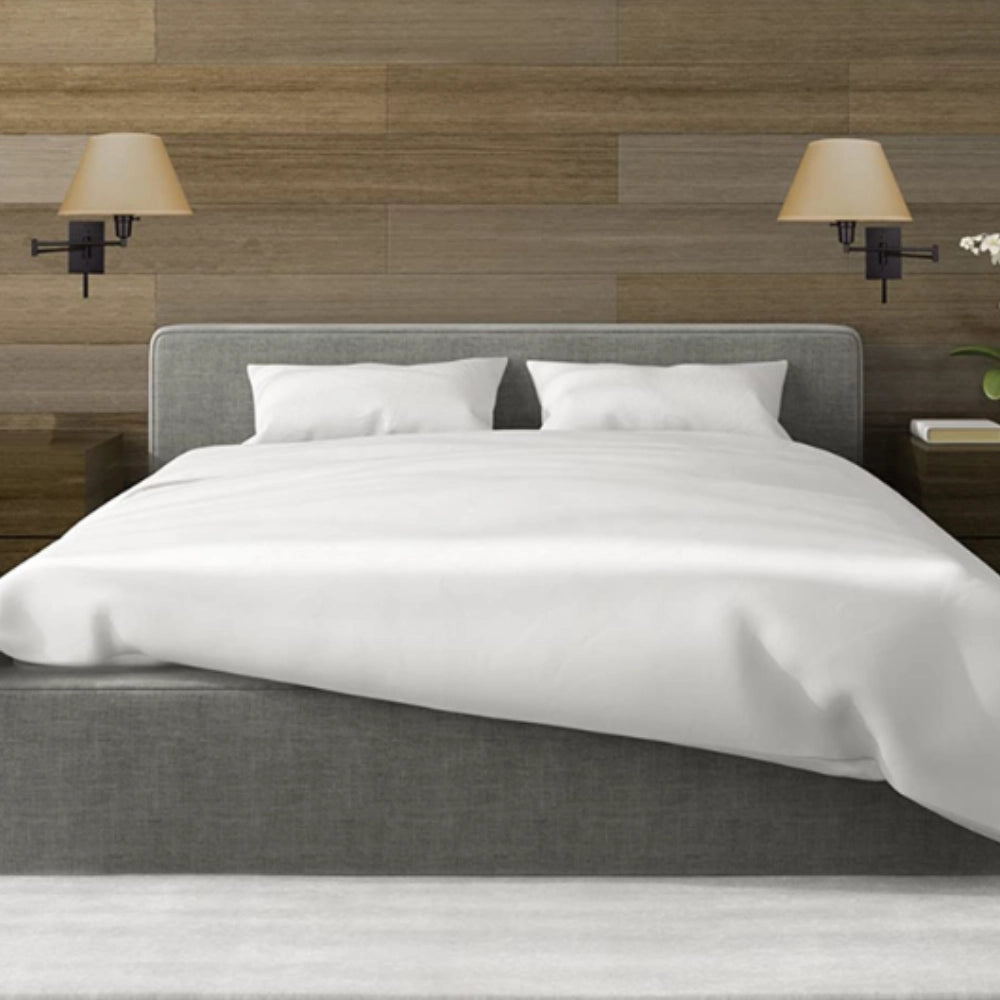 Bronze adjustable modern wall sconce with a luxury swing arm lamp design, mounted above a grey bed frame with pillows, providing ambient light in a contemporary bedroom setting.