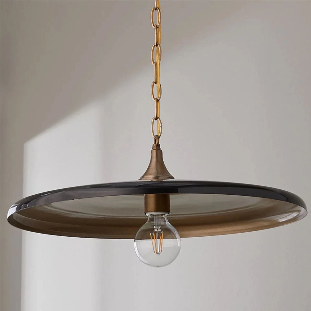 Bronze minimalist circular metal pendant light with an adjustable chain, featuring an amber-tinted glass shade, suspended from the ceiling.