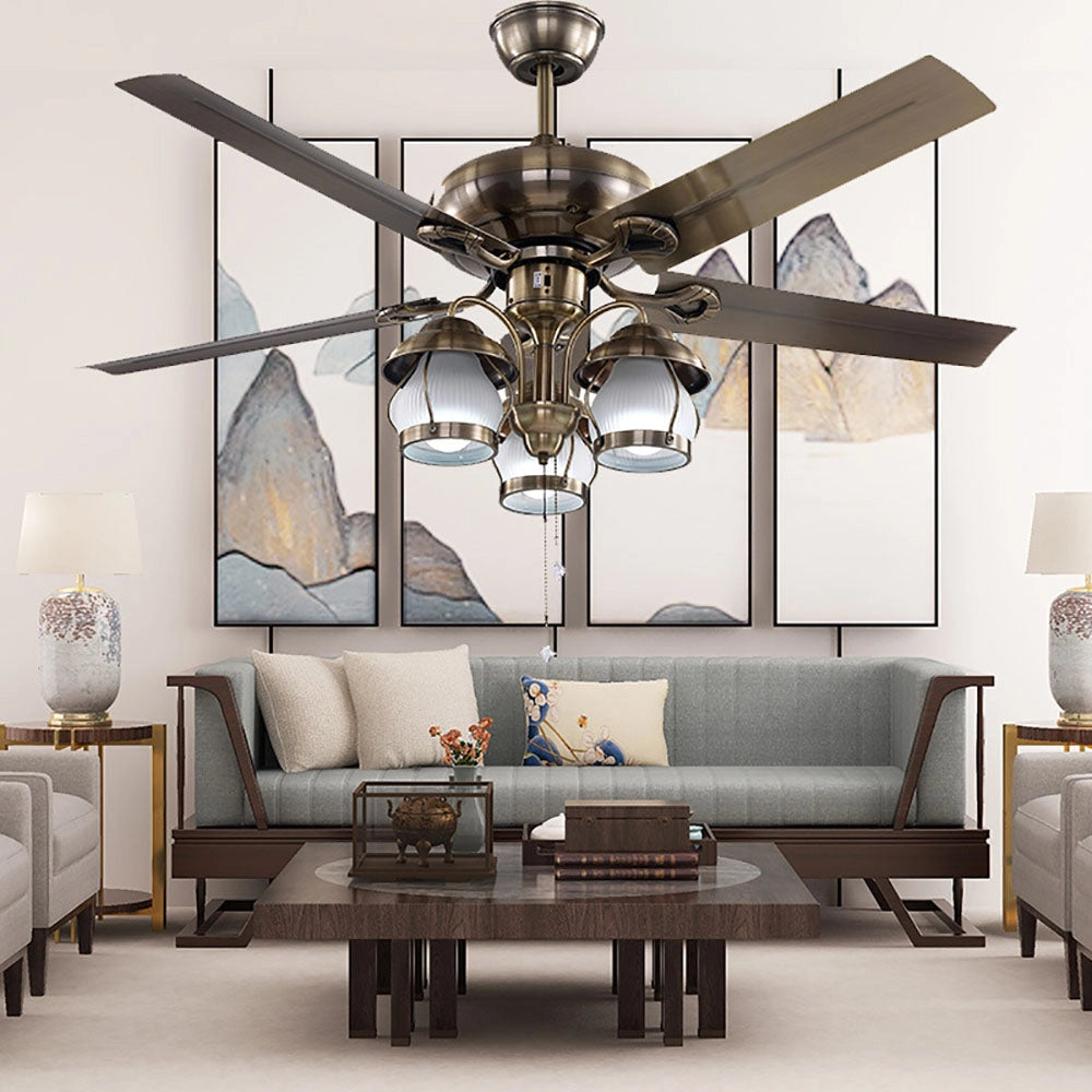 Brushed nickel 5-blade ceiling fan with lights and pull chain in an indoor setting, featuring three light heads, mounted on a ceiling in a room with modern interior design elements including a white couch, picture frames, and wooden flooring.