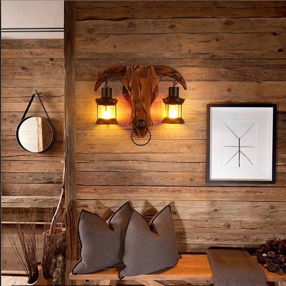Western rustic outdoor wall light featuring a dual lantern design with a bull head motif, mounted on a wooden wall, illuminating the surrounding area.