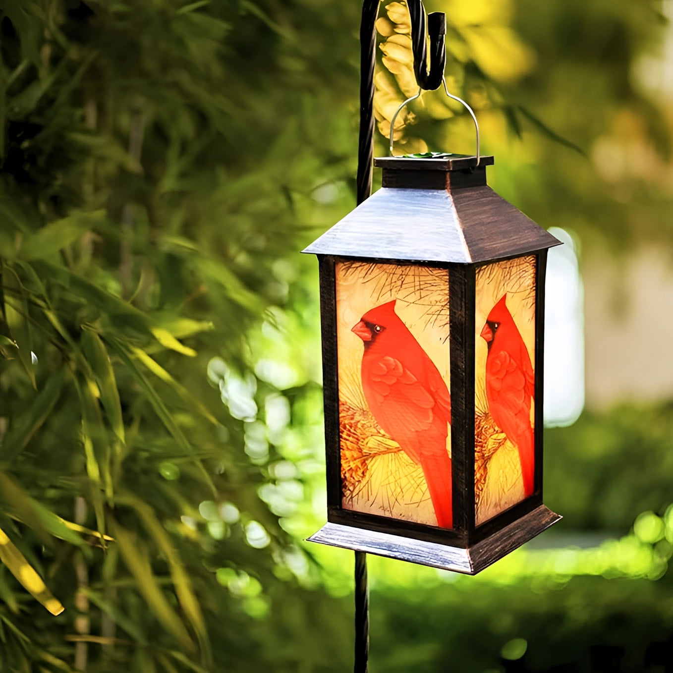 Rustic outdoor hanging lantern featuring a cardinal bird design, hanging on a tree branch with surrounding grass and plants.