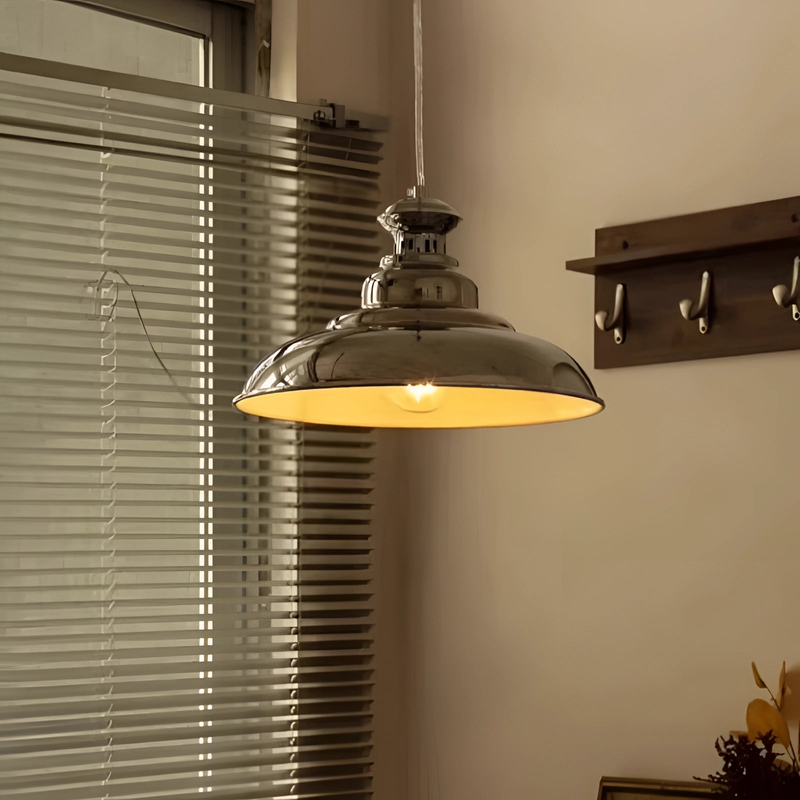 Chrome pendant light with a modern industrial dome design, featuring an adjustable chain. The light is displayed against a wooden background with plants in the vicinity.