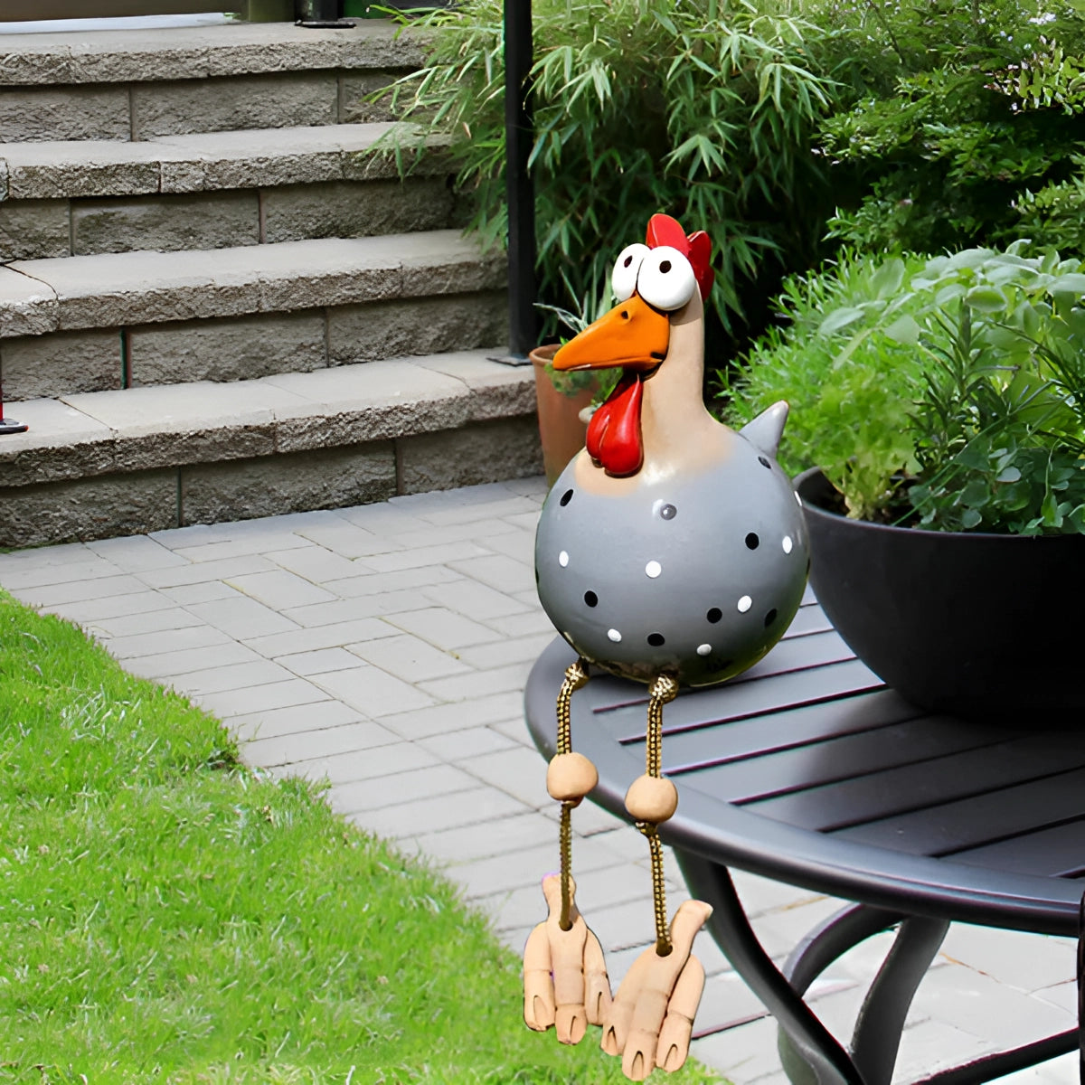 Gray metal garden chicken sculpture placed on grass, surrounded by plants, featuring a quirky design as part of outdoor decor.