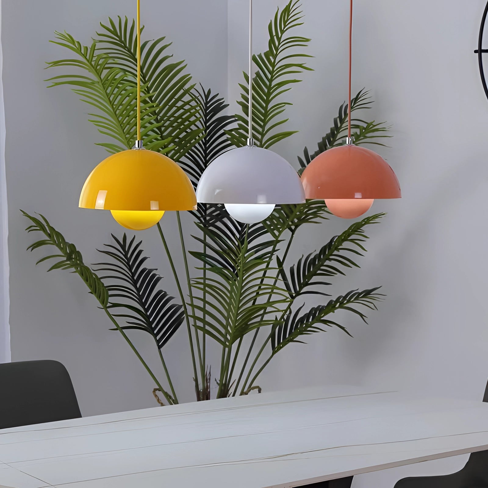 Modern dining room with colorful pendant lights hanging above a rectangular table, surrounded by green plants and Scandinavian decor elements.
